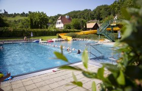 Freibad mit gelber Rutsche, umgeben von grüner Landschaft und Häusern., © Donau_Niederoesterreich_Barbara_Elser