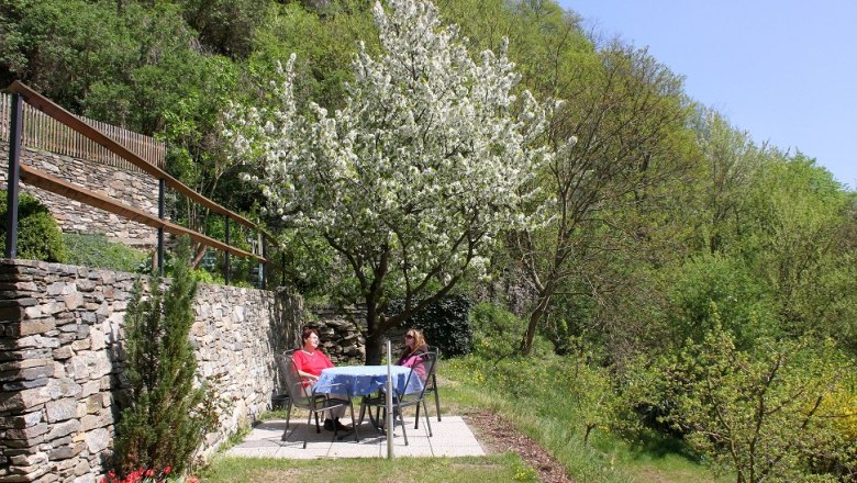 Zwei Personen sitzen an einem Tisch im Garten unter einem blühenden Baum., © Bergkirchner