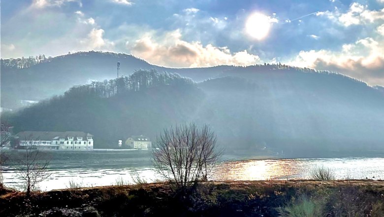 Sonniger Fluss mit Hügeln und Gebäuden im Hintergrund, klare Himmel., © Haus Donau, Hr. Benesics